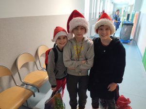 Trzech uczniów klasy piątej pozuje do wspólnego zdjęcia w czapeczkach świętego Mikołaja.