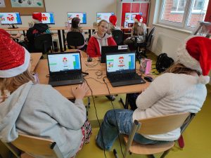 Uczniowie klasy szóstej siedzą przed laptopami w sali informatycznej. Na ekranach widać tworzoną przez uczennice postać świętego Mikołaja.