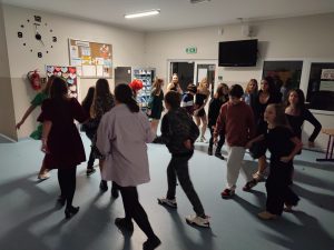 Uczniowie tańczą w parach na szkolnym korytarzu. Pary ustawione są po okręgu.