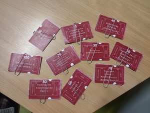 zdjęcie rozłożonych obok siebie i pospinanych spinaczami kuponów z opisami nagród w loterii i numerem losu. Na widocznych kuponach napisy: "Uśmiech Pani Agnieszki Perduty-Pilarskiej", "DODATKOWA POPRAWA SPRAWDZIANU", "Przesunięcie klasówki na kolejną lekcję przyrody", "Poprawa dowolnej oceny" , "Zwolnienie z kartkówki", "Dodatkowe nieprzygotowanie", "Napisanie pracy pisemnej z podręcznikiem/atlasem/zeszytem ćwiczeń", "Dodatkowe nieprzygotowanie", ""Porcja ciasta w kawiarence", ""Poprawa oceny i wykreślenie poprzedniej".