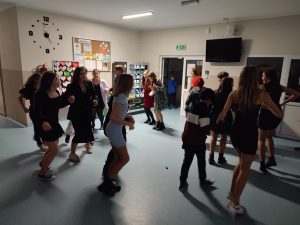 Uczniowie tańczą w parach na szkolnym korytarzu. Pary ustawione są po okręgu.