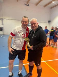 Dwóch zawodników pozuje do wspólnego zdjęcia. Jeden z nich trzyma puchar.