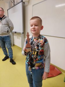 Uczeń klasy drugiej stoi trzymając w dłoni puchar. w tle widać fragment stojącego pana Kamińskiego.