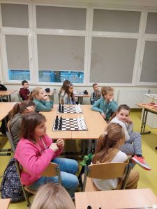 Uczniowie klasy drugiej siedzą wokół stołu, na którym rozstawione są dwie szachownice.
