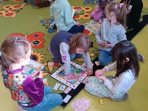 Uczniowie grają na dywanie w leżącą przed nimi grę monopoly.