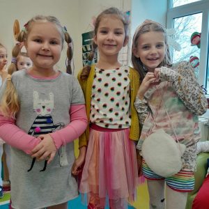 Trzy dziewczynki z oddziału przedszkolnego pozują do wspólnego zdjęcia. Uczennice się uśmiechają. Jedna z nich układa przed sobą dłonie w kształcie serduszka.
