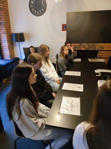 Uczennice klasy siódmej siedzą przy długim stole. Przed dziewczynkami leżą zafoliowane i przyklejone do stołu kartki papieru.