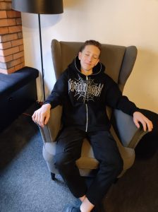 Uczeń klasy siódmej siedzi wygodnie na fotelu z zamkniętymi oczami. Chłopiec uśmiecha się.