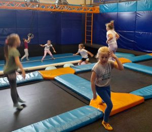 Uczniowie oddziału przedszkolnego skaczą na trampolinach. W tle widać grające i biegające dzieci.