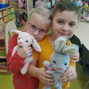 Dwoje uczniów oddziału przedszkolnego przytulają się. Dzieci trzymają w dłoniach pluszowe króliczki.