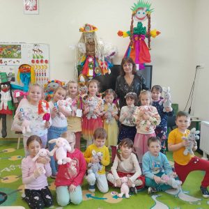 Uczniowie oddziału przedszkolnego pozują do wspólnego zdjęcia wraz ze swoją wychowawczynią. Dzieci przytulają pluszowe króliczki. W tle widać dwie duże kukły - marzanny.