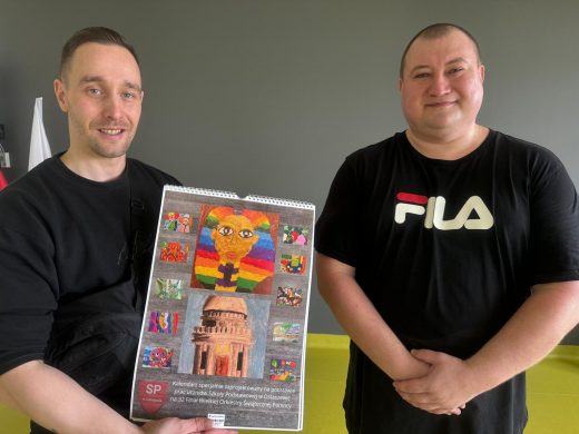 Zaproszenie raperzy pozują do wspólnego zdjęcia. Jeden z nich trzyma w dłoni kalendarz ścienny z pracami naszych uczniów.