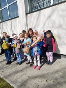 Uczniowie klasy drugiej pozują do wspólnego zdjęcia przy ścianie szkoły. Dzieci trzymają w dłoniach znalezione prezenty.