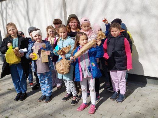Uczniowie klasy drugiej pozują do wspólnego zdjęcia przy ścianie szkoły. Dzieci trzymają w dłoniach znalezione prezenty.