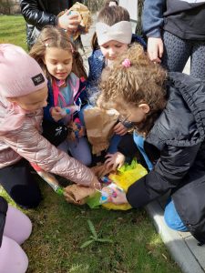 Uczennice klasy drugiej pochylają się nad leżącym na ziemi żółtym workiem z upominkami dla dzieci. Dziewczynki wyciągają i oglądają umieszczone w środku prezenty.