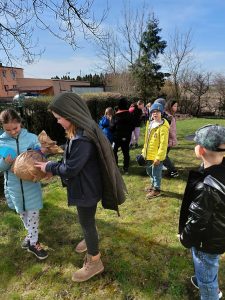 Uczniowie klasy drugiej stoją na trawniku. Dziewczynki widoczne na pierwszym planie oglądają piłkę zapakowaną w brązowy papier.