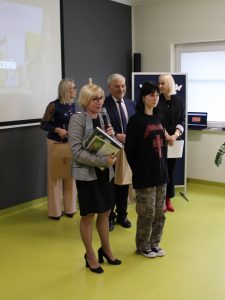 Na środku sali stoją Pani Dyrektor wraz z nagrodzoną w konkursie uczennicą oraz Pan Wójt Gminy Łysomice i dwie nauczycielki. Pani Dyrektor trzyma w jednej dłoni mikrofon a w drugiej książkę i dyplom dla dziewczyny