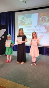 Trzy uczennice stoją na scenie trzymając dłoniach przed sobą dyplomy.