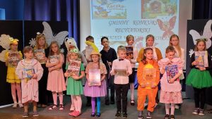 Uczniowie nagrodzeni w konkursie stoją na scenie. Dzieci trzymają w dłoniach książki.