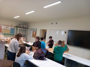 Uczniowie stoją w klasie przy długich ławkach i przygotowuję zbroje rycerskie.