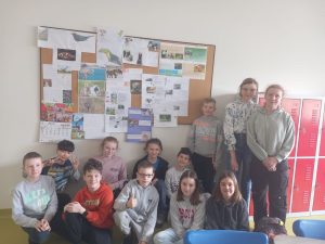 Uczniowie pozują do wspólnego zdjęcia przy tablicy na której umieszczone zostały przygotowane przez nich projekty dotyczące zwierząt.