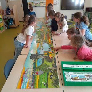 Uczniowie oddziału przedszkolnego pochylają się nad długą, kolorową planszą rozłożoną na stole