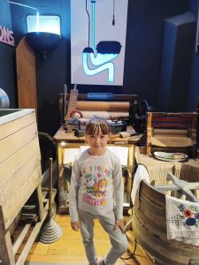 Uczennica pozuje do zdjęcia stojąc na tle schematu zawieszonego na ścianie za nią. Schemat przedstawia spłuczkę i spływającą wodę.