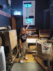 Uczennica pozuje do zdjęcia wskazując na schemat zawieszony na ścianie za nią. Schemat przedstawia spłuczkę i spływającą wodę.