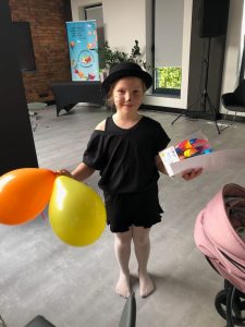 Uczennica nagrodzona w konkursie stoi trzymając w jednej dłoni balony a w drugiej dyplom i otrzymaną nagrodę.