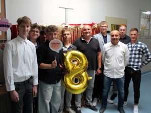 Uczniowie klasy ósmej pozują do wspólnego zdjęcia ze swoimi nauczycielami. Jeden z chłopców trzyma przed sobą złoty balon w kształcie cyfry 8, a uczeń stojący obok tabliczkę z napisem "ZROBILIŚMY TO".