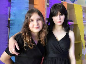 Dwie uczennice klasy ósmej pozują do wspólnego zdjęcia podczas balu. Jedna z dziewcząt obejmuje koleżankę.