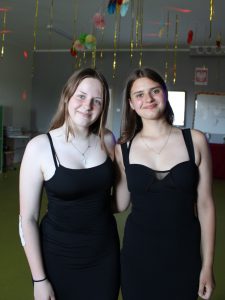 Dwie uczennice klasy ósmej pozują do wspólnego zdjęcia podczas balu. Dziewczynki się uśmiechają i obejmują.