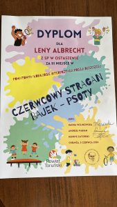 Zdjęcie dyplomu otrzymanego przez uczennicę szkoły. Na dyplomie widoczne są grafiki uśmiechniętych dzieci oraz kolorowe kleksy. Na nich napisy: "DYPLOM DLA LENY ALBRECHT Z SP W OSTASZEWIE ZA III MIEJSCE W POWIATOWYM KONKURSIE POEZJI DZIECIĘCEJ CZERWCOWY STRAGAN BAJEK - PSOTY JURY: HANNA WOJNOWSKA ANDRZEJ PABIAN HENRYK ZATORSKI CHEŁMŻA, 5 CZERWCA 2024".