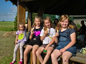 Cztery uczennice siedzą na drewnianej ławeczce i jedzą lody.