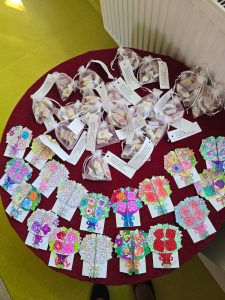 Zdjęcie przygotowanych przez uczniów podarunków dla rodziców. Na okrągłym stole leżą ułożone laurki i paczuszki ze słodyczami z doczepionymi liścikami.