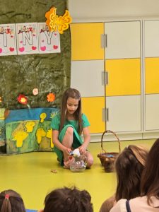 Uczennica kuca na podłodze. Przed nią stoi szklane naczynie, z którego wyciąga mały przedmiot.