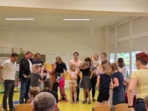 Uczniowie wraz z rodzicami stoją na środku sali. Dzieci przytulają się do swoich rodziców.