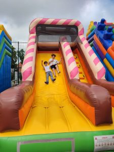 Dwoje uczniów zjeżdża z kolorowego dmuchańca. Chłopcy trzymają się za dłonie.