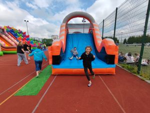 Uczeń biegnie przed dmuchańcem. Za nim widoczny jest jego kolega zjeżdżający z niego.