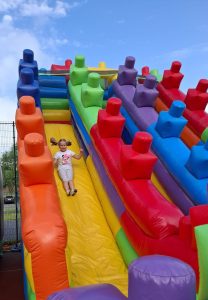 Uczennica zjeżdża z dmuchańctwa. Ma włosy związane w dwa kitki, które podnoszą sięna bok.