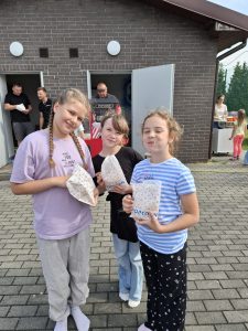 Trzy uczennice pozują do wspólnego zdjęcia trzymając przed sobą torebki z popcornem.