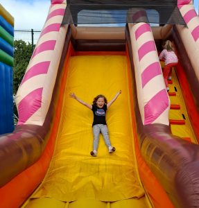 Uczennica zjeżdża z dmuchańca z otwartą buzią szeroko rozstawiając ręce.