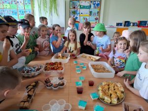 Uczniowie stoją wokół stołu, na którym rozłożone są słodkie przekąski.