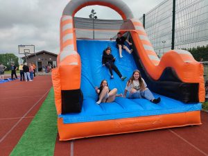 Czworo uczniów zjeżdża z dmuchańca. Dzieci się śmieją.