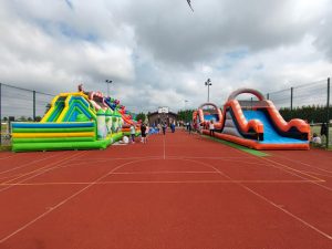 Zdjęcie ustawionych na czerwonej murawie boiska w dwóch rzędach dmuchańców.