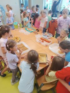 Uczniowie stoją wokół stołu, na którym ustawione są słodkie przekąski.