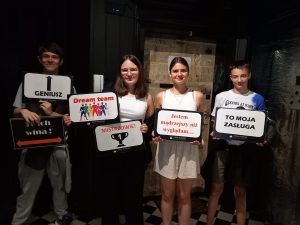 Czworo uczniów klasy VII pozuje do zdjęcia trzymając w dłoniach tabliczki z napisami: "Geniusz", "To ich wina !", "Dream team", "MISSTRZOWIE", "Jestem mądrzejszy niż wyglądam...", "TO MOJA ZASŁUGA".