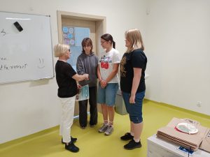 Pani Dyrektor stoi z dyplomem na przeciwko jednej z drużyn biorących udział w konkursie i ściska dłoń jednej z uczennic.