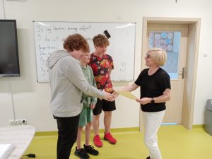 Pani Dyrektor stoi na przeciwko trzech uczniów naszej szkoły. W jednej dłoni trzyma dyplom a drugą wyciąga w kierunku jednego z uczniów składając mu gratulacje.