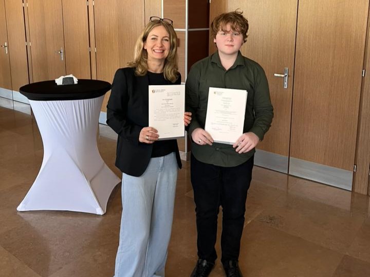 Uczeń, który otrzymał tytuł laureata w kuratoryjnym konkursie z języka angielskiego pozuje do wspólnego zdjęcia ze swoją opiekunką. Oboje trzymają przed sobą otrzymane dyplomy.